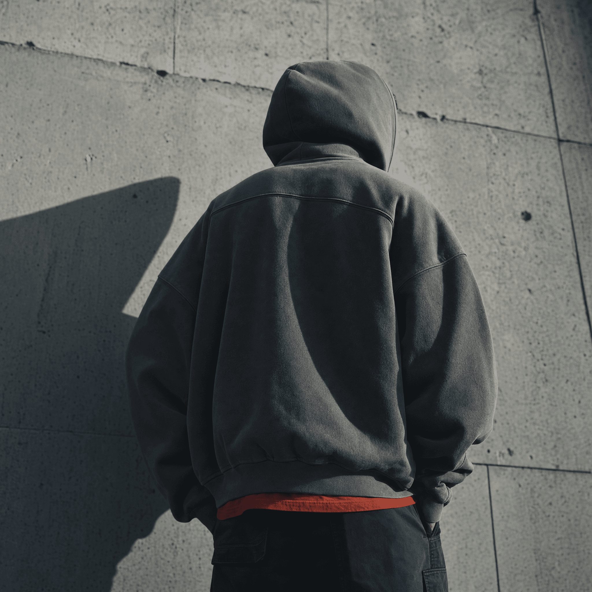 Back of the Drop 04 heavyweight hoodie, hood up, against a raw concrete wall, desaturated cinematic grade